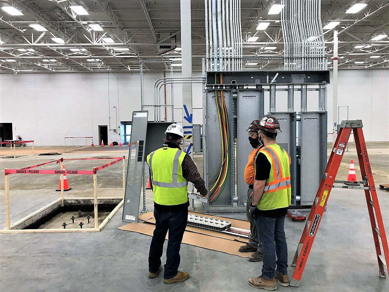 Construction team reviewing electrical equipment installation inside a building under construction.
